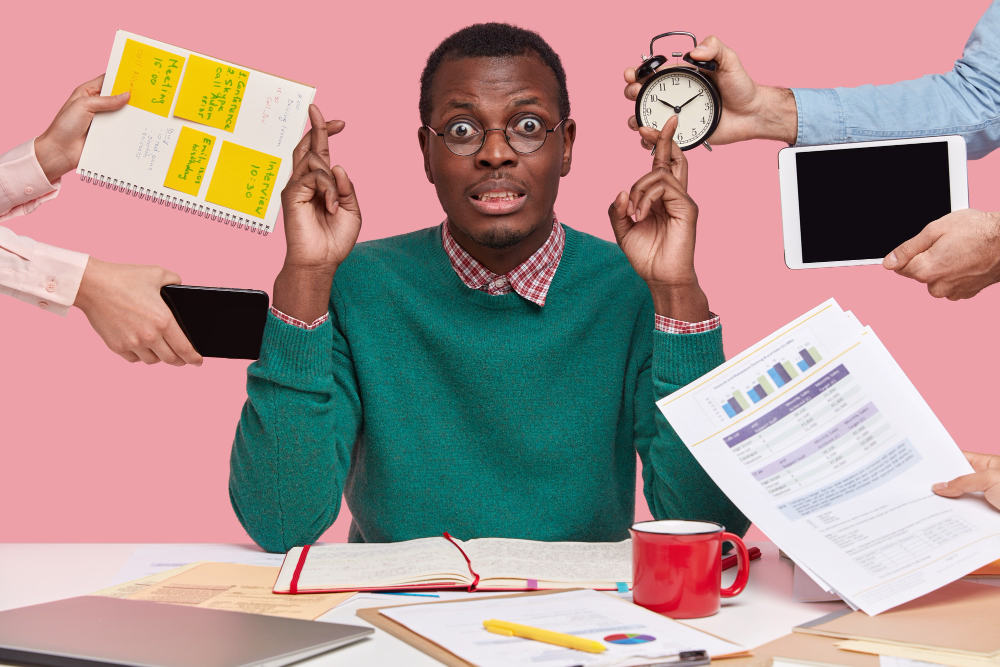 A stressed man surrounded by multiple hands holding work-related items like a clock, tablet, phone, sticky notes, and reports—visually representing the chaos and overload faced by product teams without proper product operations in place.